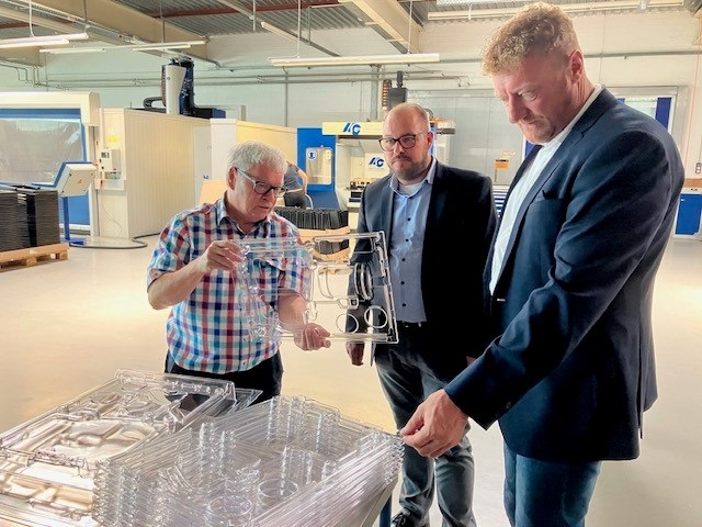 Matthias Bohl hat ein durchsichtiges Plastikteil in der Hand. Er zeigt es Sebastian Straubel und Michael Keilich.