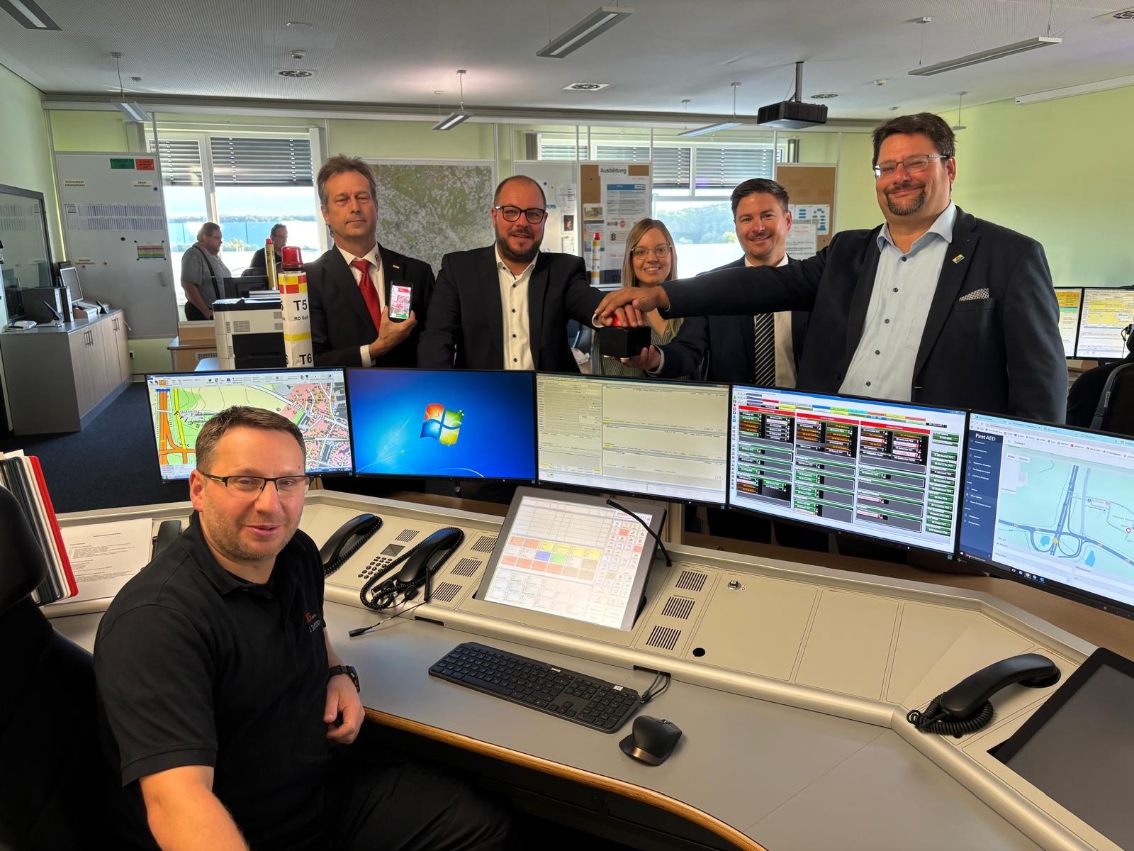 Das Projektteam Coburg für die „Region der Lebensretter“ steht an einem Computer-Arbeitsplatz in der Integrierten Leitstelle. Vorne sitzt Jan Dormann, hinter ihm stehen Peter Kunzelmann (Leiter der ILS Coburg), Stefanie Trütschel, Ralf Scheichenost (beide Zweckverband für Rettungsdienst und Feuerwehralarmierung), Verbandsrat Stefan Wicklein und Verbandsvorsitzender Sebastian Straubel.