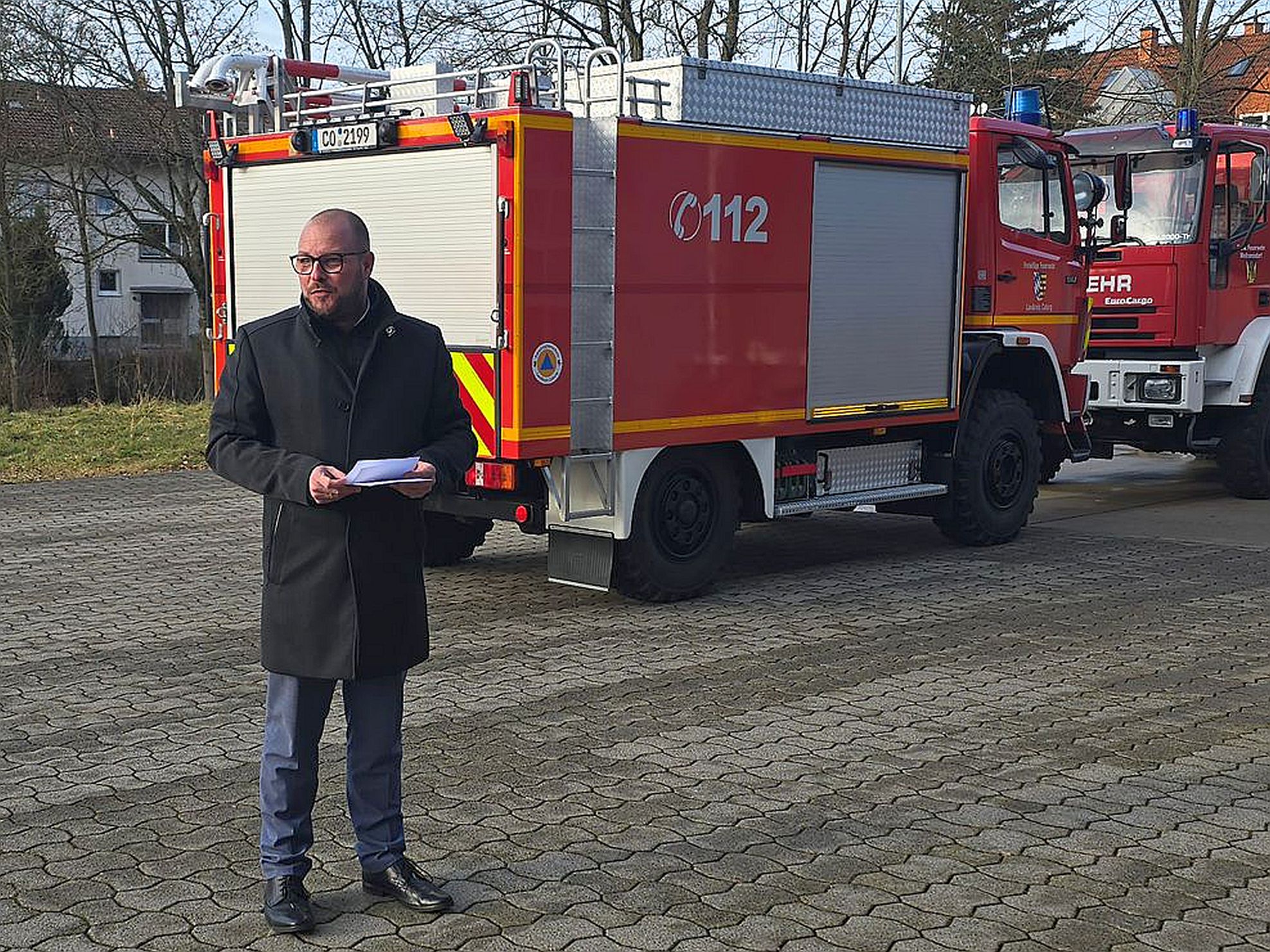 Landrat Sebastian Straubel steht vor zwei roten Feuerwehrfahrzeugen und hält eine Ansprache.