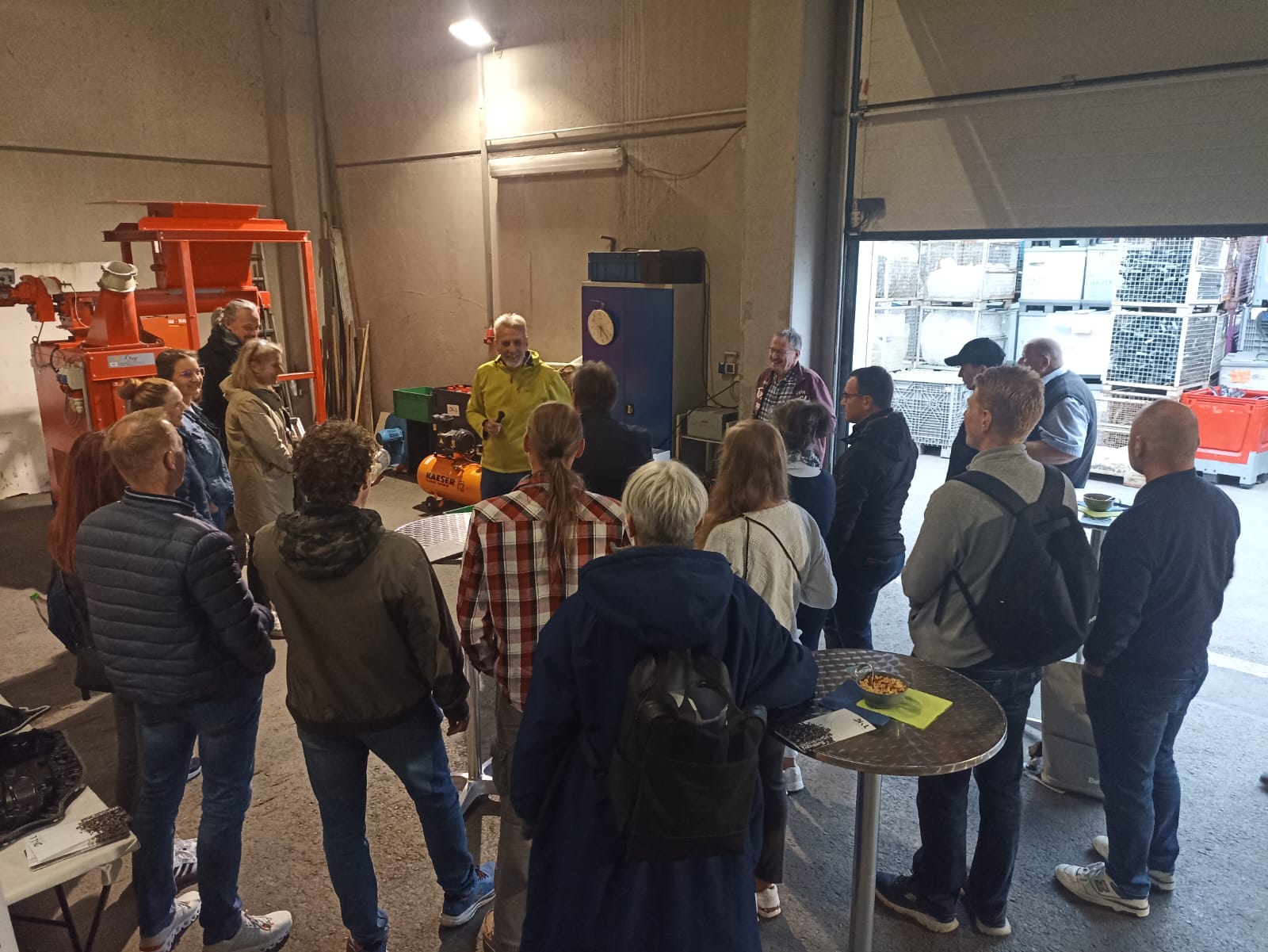 Eine Gruppe von Menschen steht in einer Fabrikhalle und folgt den Ausführungen eines Mannes vor einer Maschine.