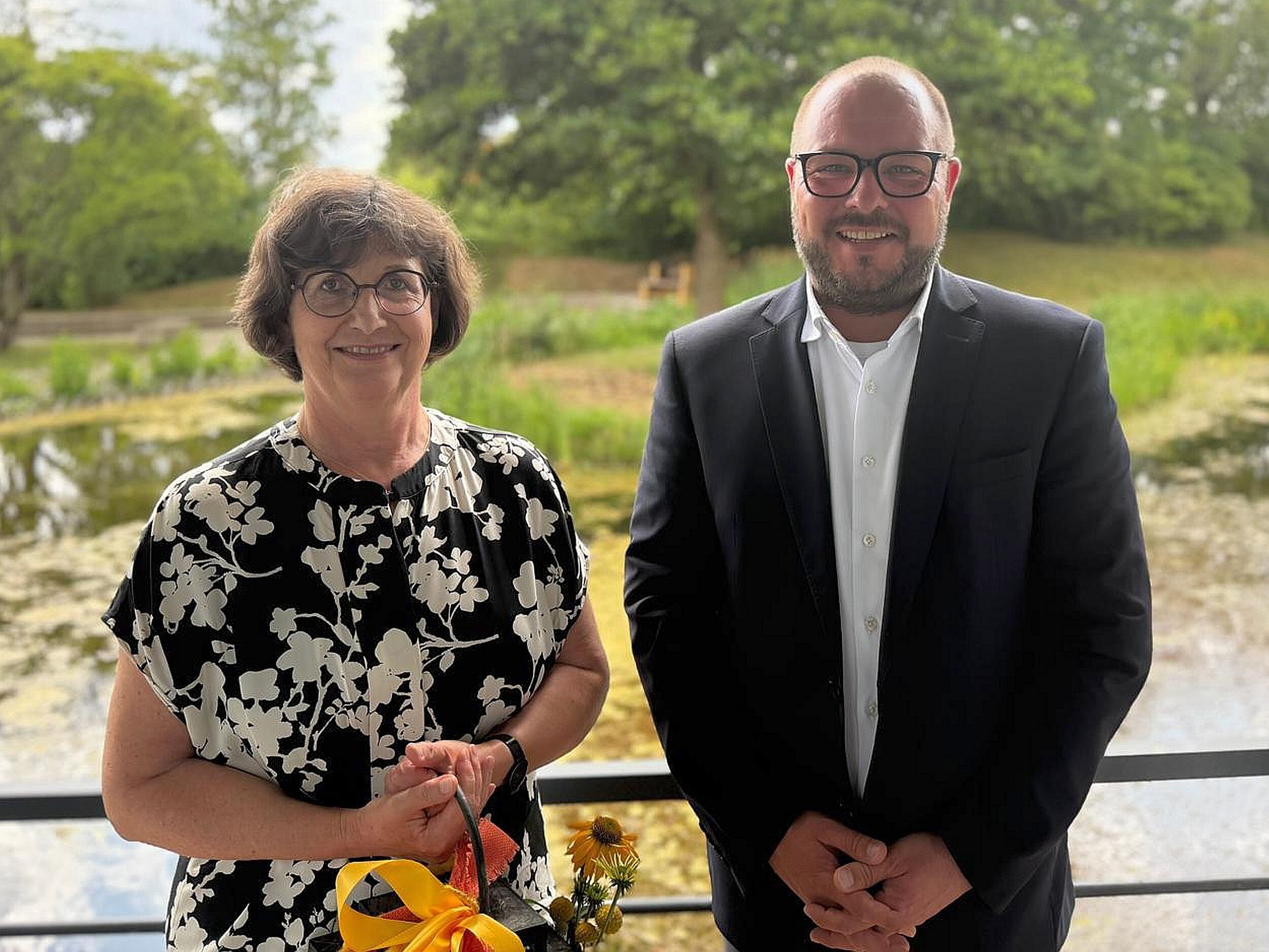 Ulrike Stadter und Landrat Sebastian Straubel stehen nebeneinander, im Hintergrund das Außengelände des Landratsamtes Coburg.