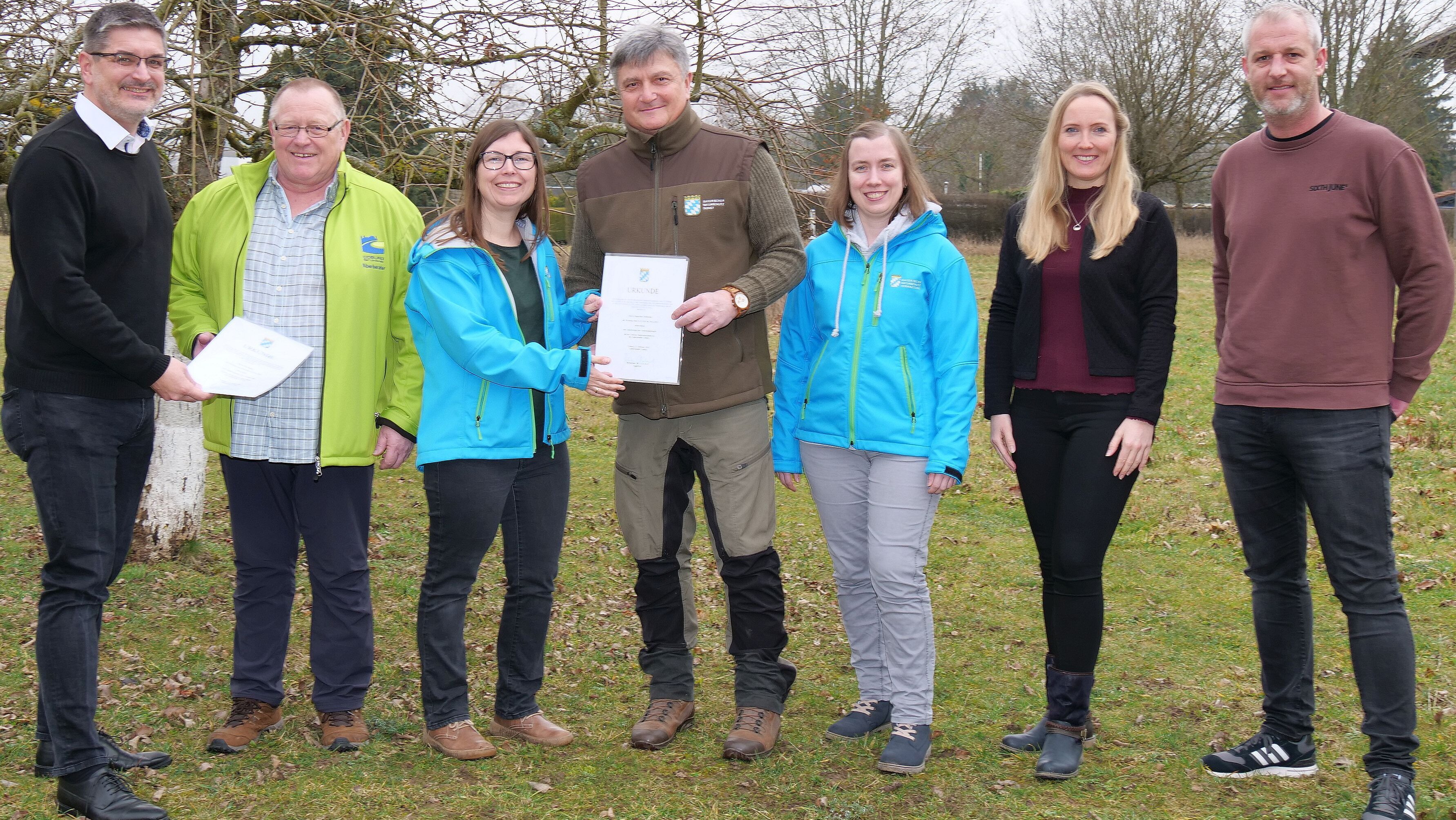 Gruppenbild mit sieben Personen in der freien Natur. In der Mitte stehen zwei Männer, die von Mitarbeitern des Landratsamtes die Bestellungsurkunden zum Naturschutzwächter überreicht bekommen.