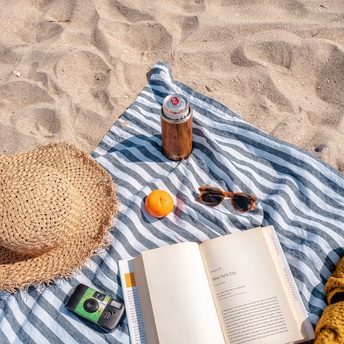 Ein Sonnenhut, ein Buch und ein Handtuch liegen am Strand - Blick aus der Vogelperspektive 