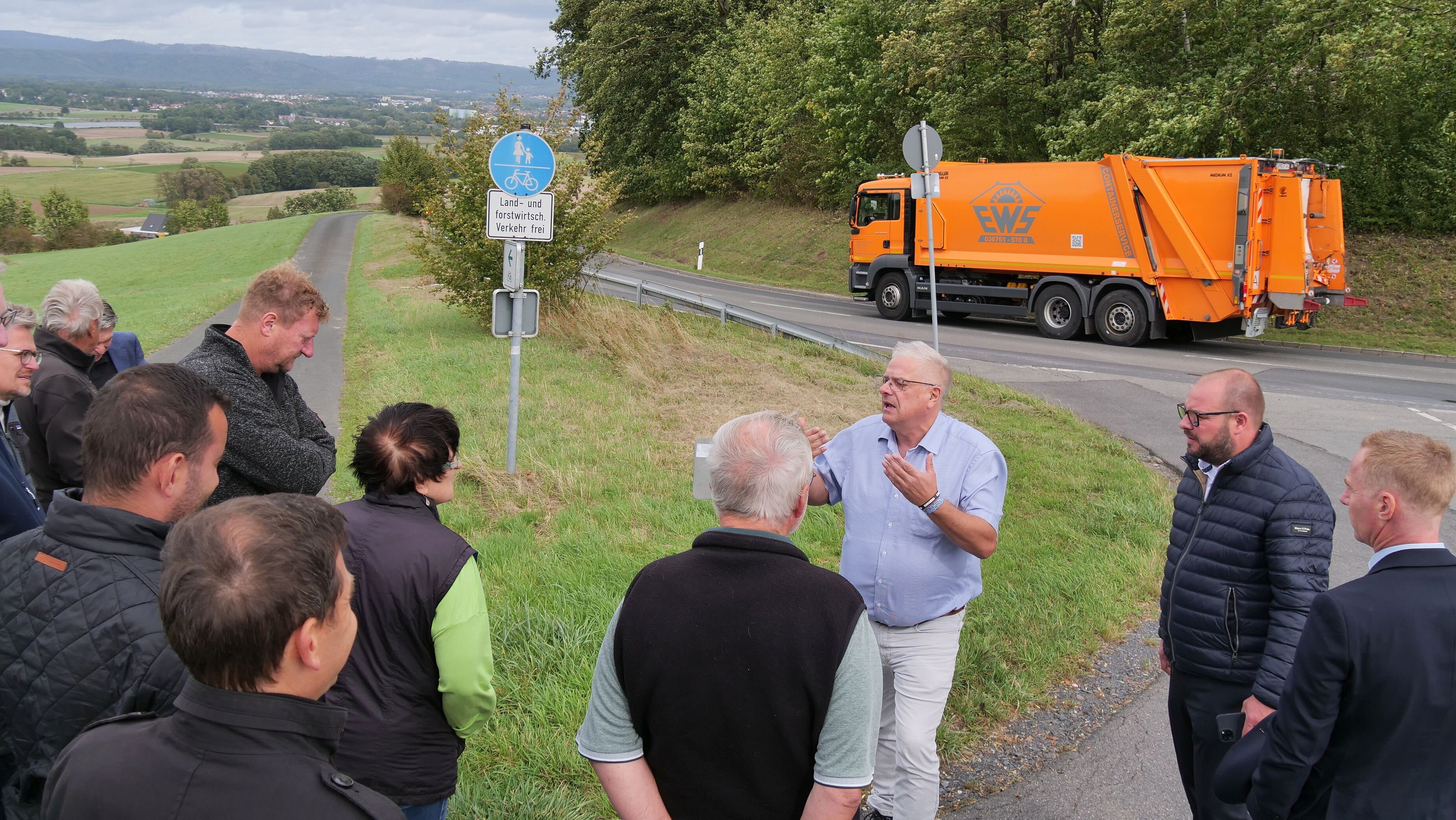 Die Mitglieder des Bauausschuss diskutieren - im Hintergrund fährt auf der Straße ein Lkw vorbei. Am Horizont sind die Stadt Neustadt sowie der Thüringer Wald zu sehen.