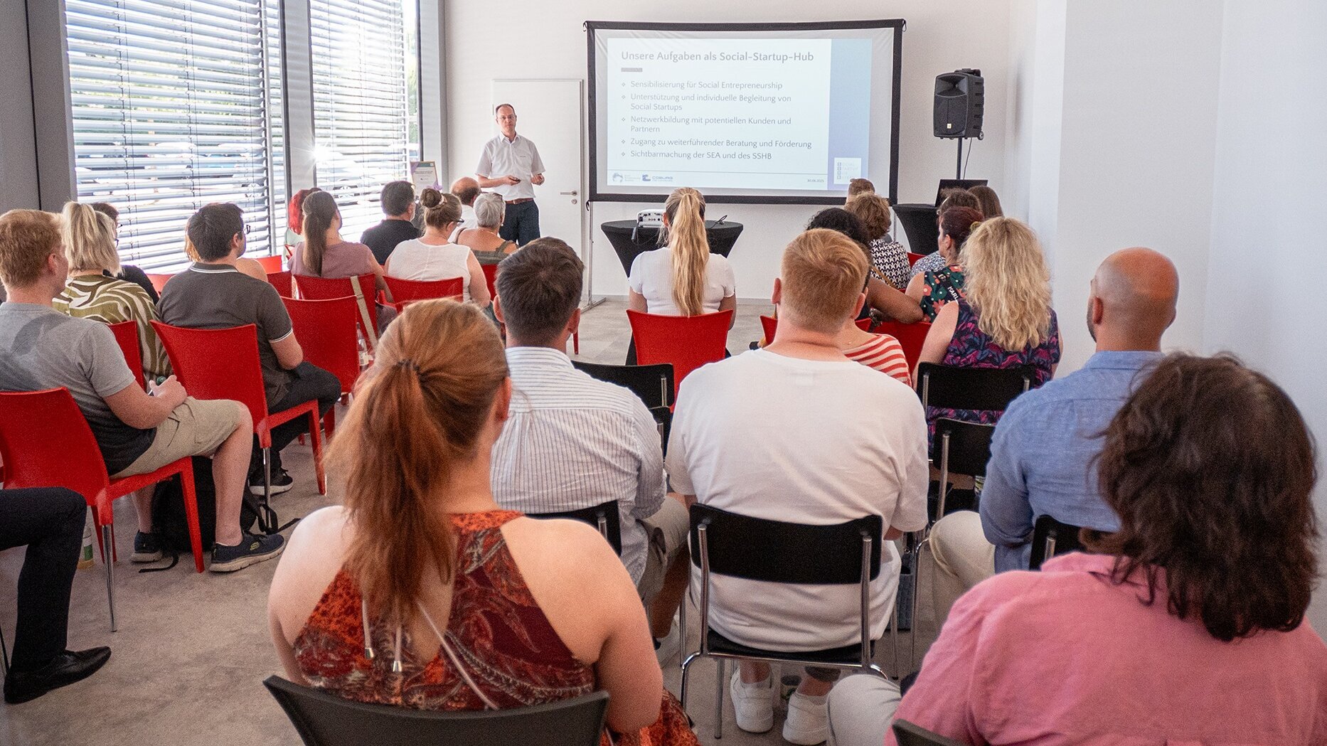 Florian Eckardt erläutert bei einer Beamer-Präsentation im Hintergrund den Besuchern der Eröffnungsveranstaltung die Aufgaben des von der Landkreis-Wirtschaftsförderung