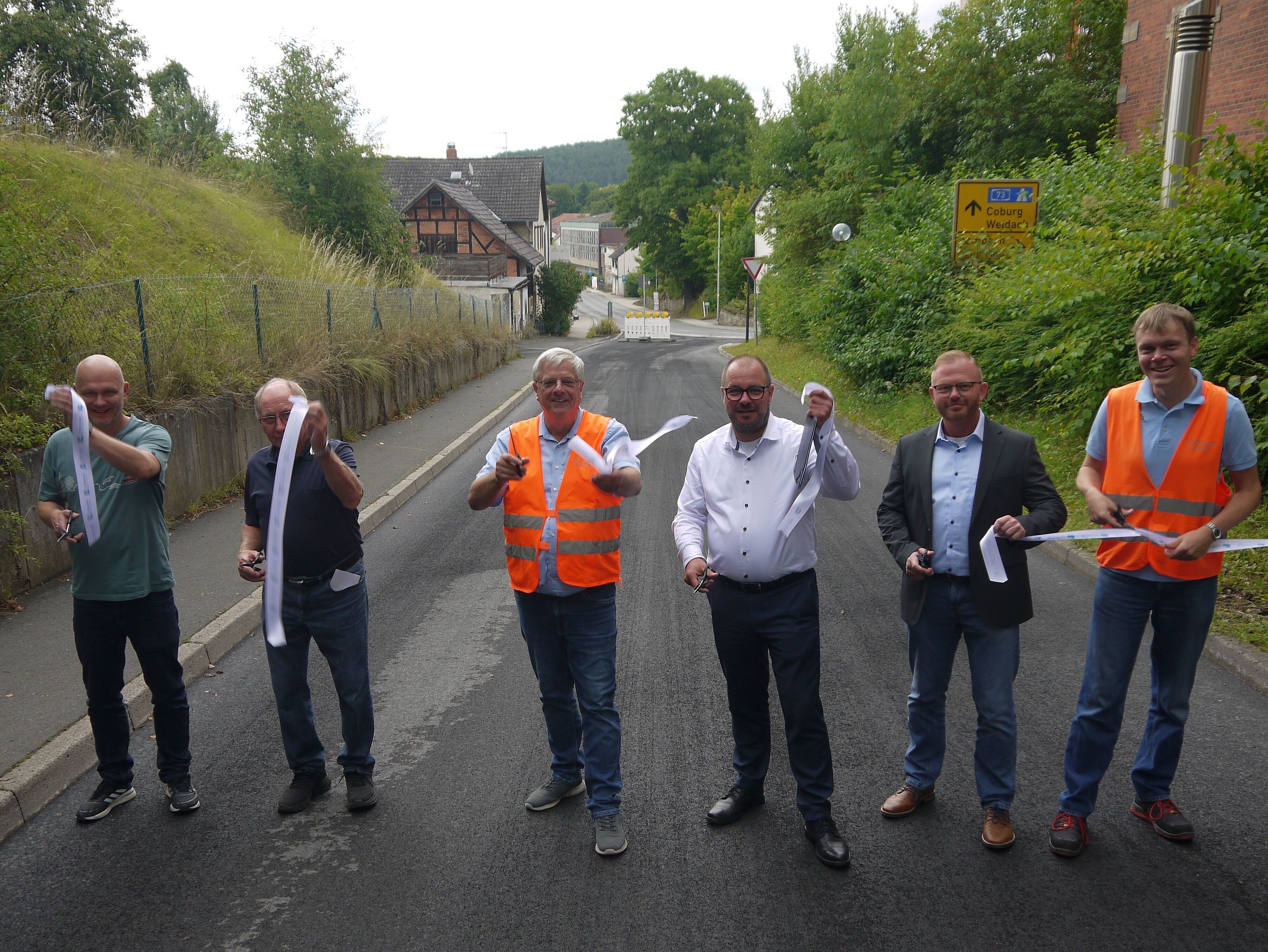 Marko Rützel, Kreisrat Gerhard Ehrlich, Jürgen Alt, Sebastian Straubel, Hans Steinfelder und Patrick Mohr schneiden vor dem Weitramsdorfer Rathaus ein Band mit dem Logo des Landkreises durch. Das ist der symbolische Akt zur Freigabe der Straße.