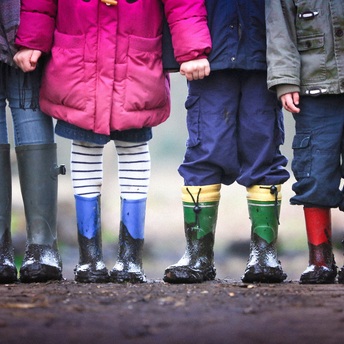 Vier Kinder stehen in bunten Gummistiefeln auf einem Feldweg