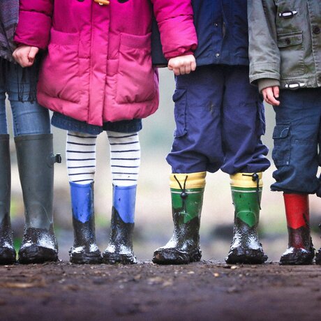 Vier Kinder stehen in bunten Gummistiefeln auf einem Feldweg