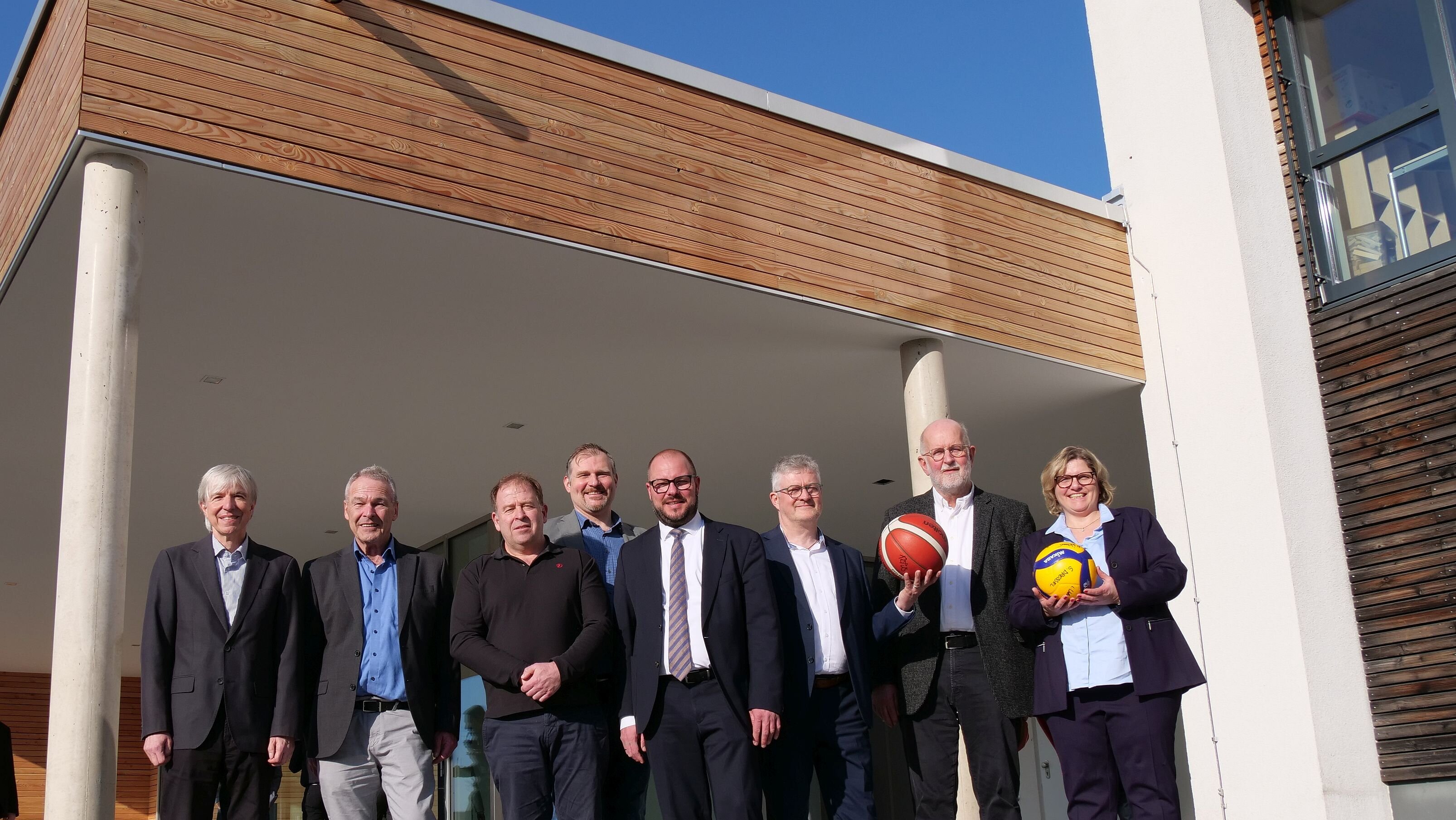 Gruppenbild mit den Ehrengästen der Einweihung. Eine Person hält einen Basketball, eine Person einen Volleyball als Geschenk für die Schulen in der Hand.