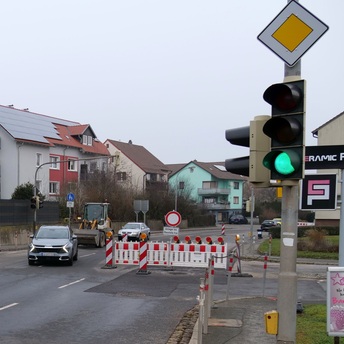 Auf der Straße der Ortsdurchfahrt in Dörfles-Esbach stehen noch Absperrbaken und Warnschilder, an denen Autos vorbeifahren. Eine Ampel am rechten Bildrand zeigt grünes Licht.