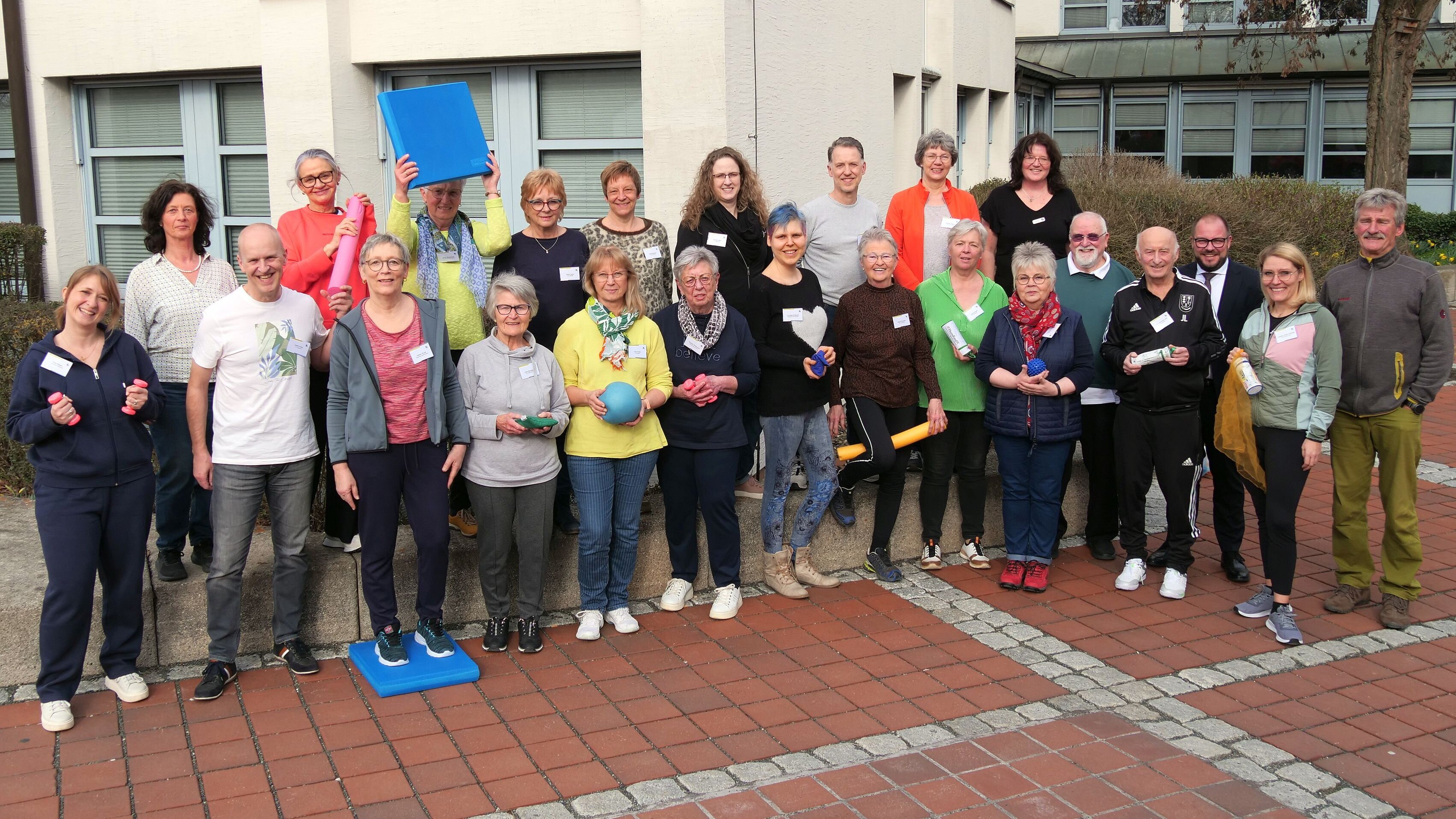 Eine Gruppe von Personen, die Bälle, Gumminudeln und kleine Hanteln für den Sport mit Senioren in der Hand halten.