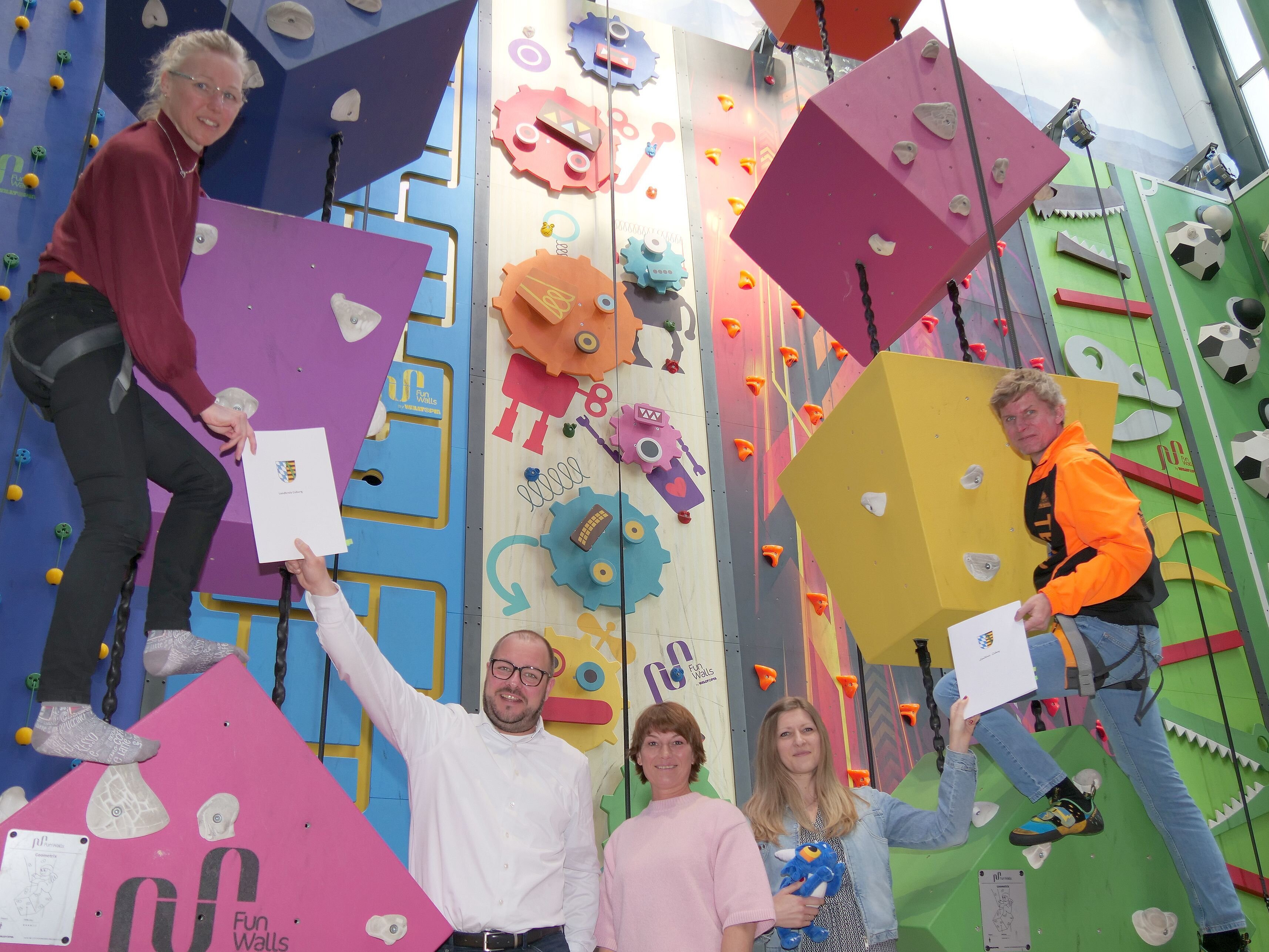 Im bunten Klettergarten der Funtasyworld hängen Stine Michel und Martin Lüders in Sicherungsseilen und reichen zwei Verträge an Sebastian Straubel und Yvonne Schnapp.