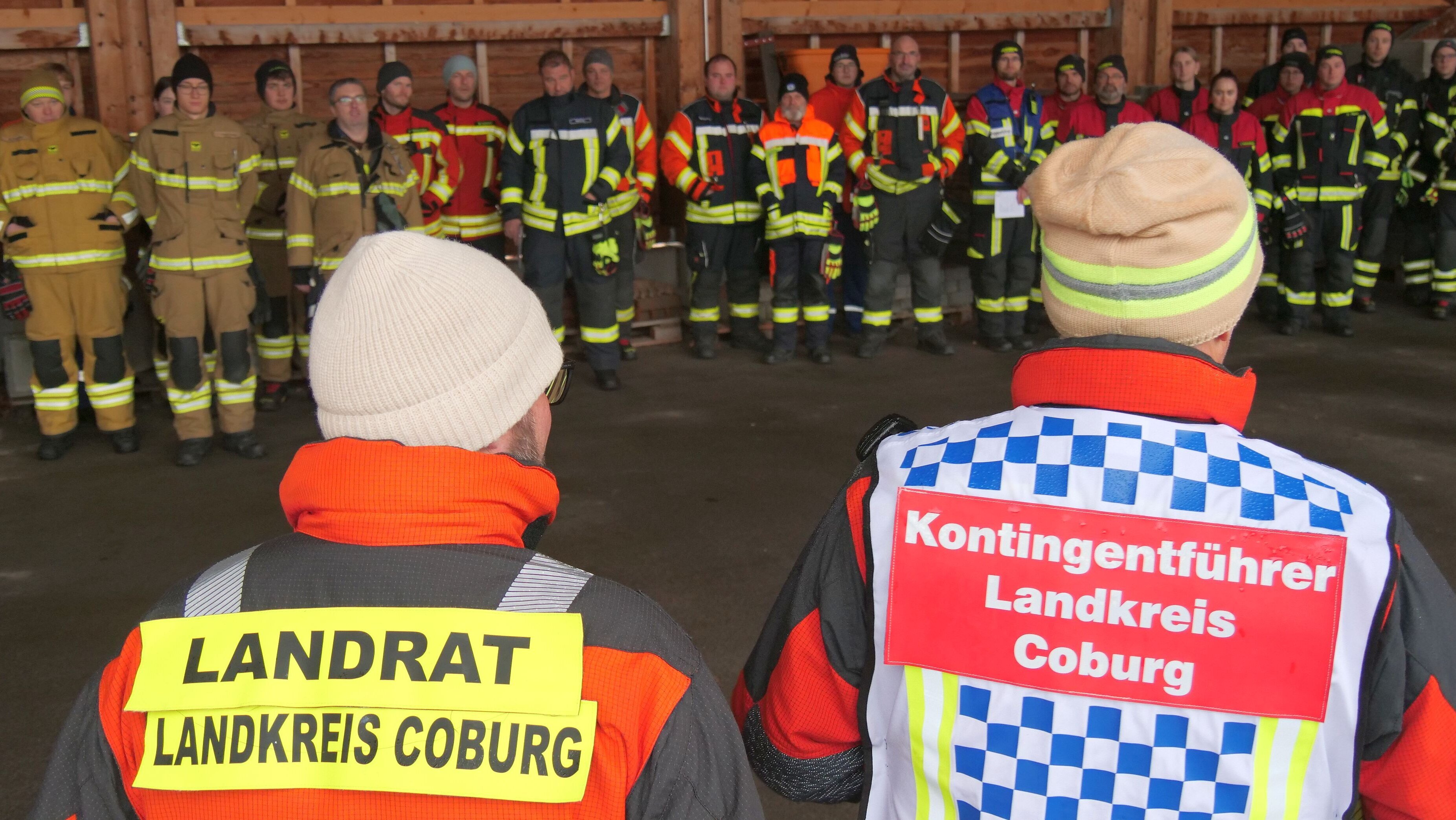 Landrat Sebastian Straubel und Stefan Püls stehen vor einer größeren Gruppe von Personen mit Feuerwehr-Einsatzkleidung.