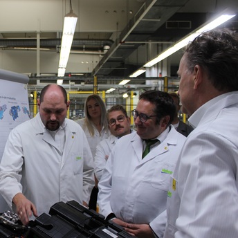 Bekleidet mit weißen Schutzjacken begutachten Staatssektretär Tobias Gotthardt und weitere Personen schwarze Kunststoffteile, die bei der Herstellung von Fahrzeugkomponenten benötigt werden.