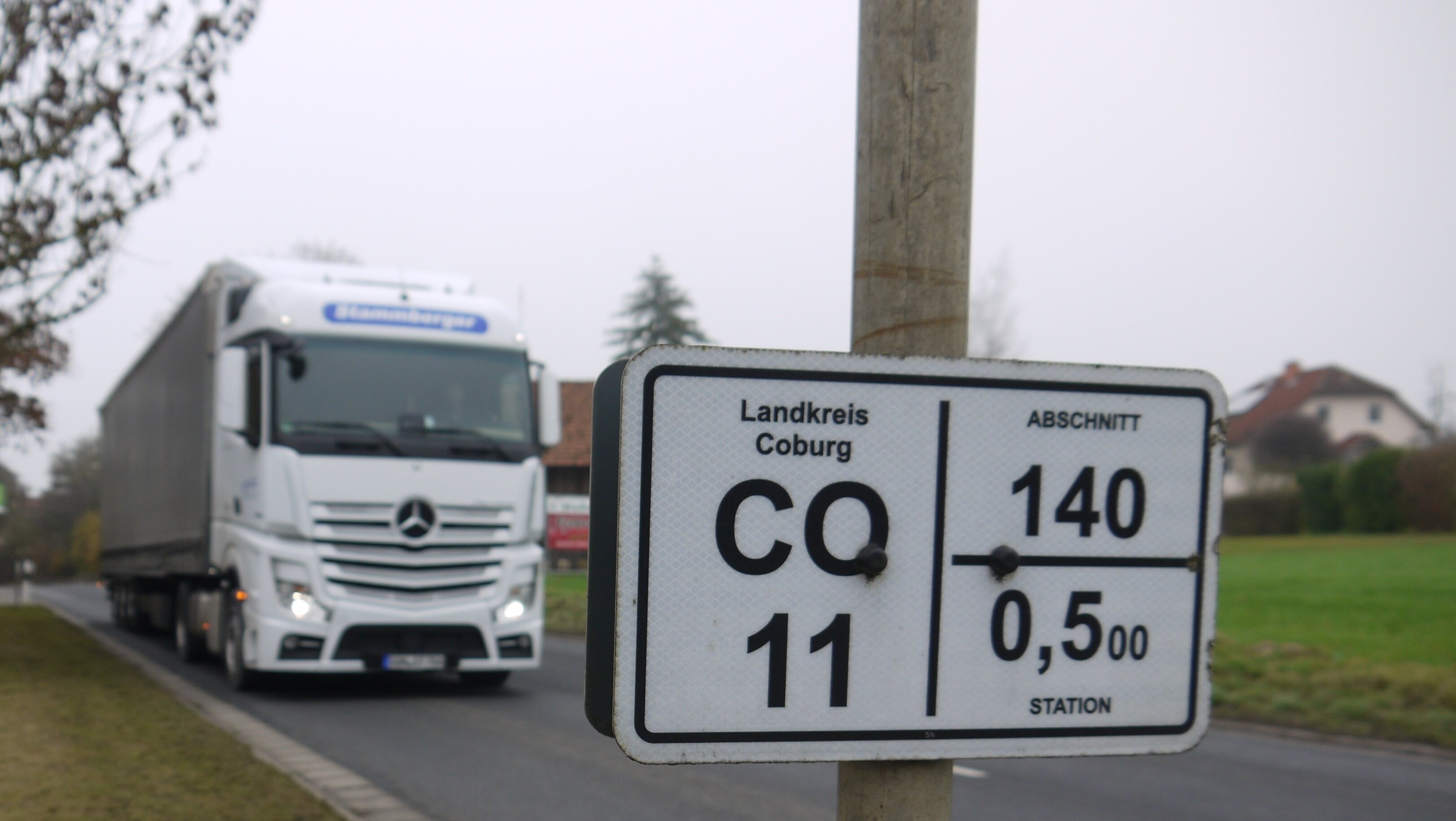 Ein weißer Lkw fährt auf einer Straße, im Vordergrund ist das Straßenschild mit der Aufschrift CO 11 zu sehen.