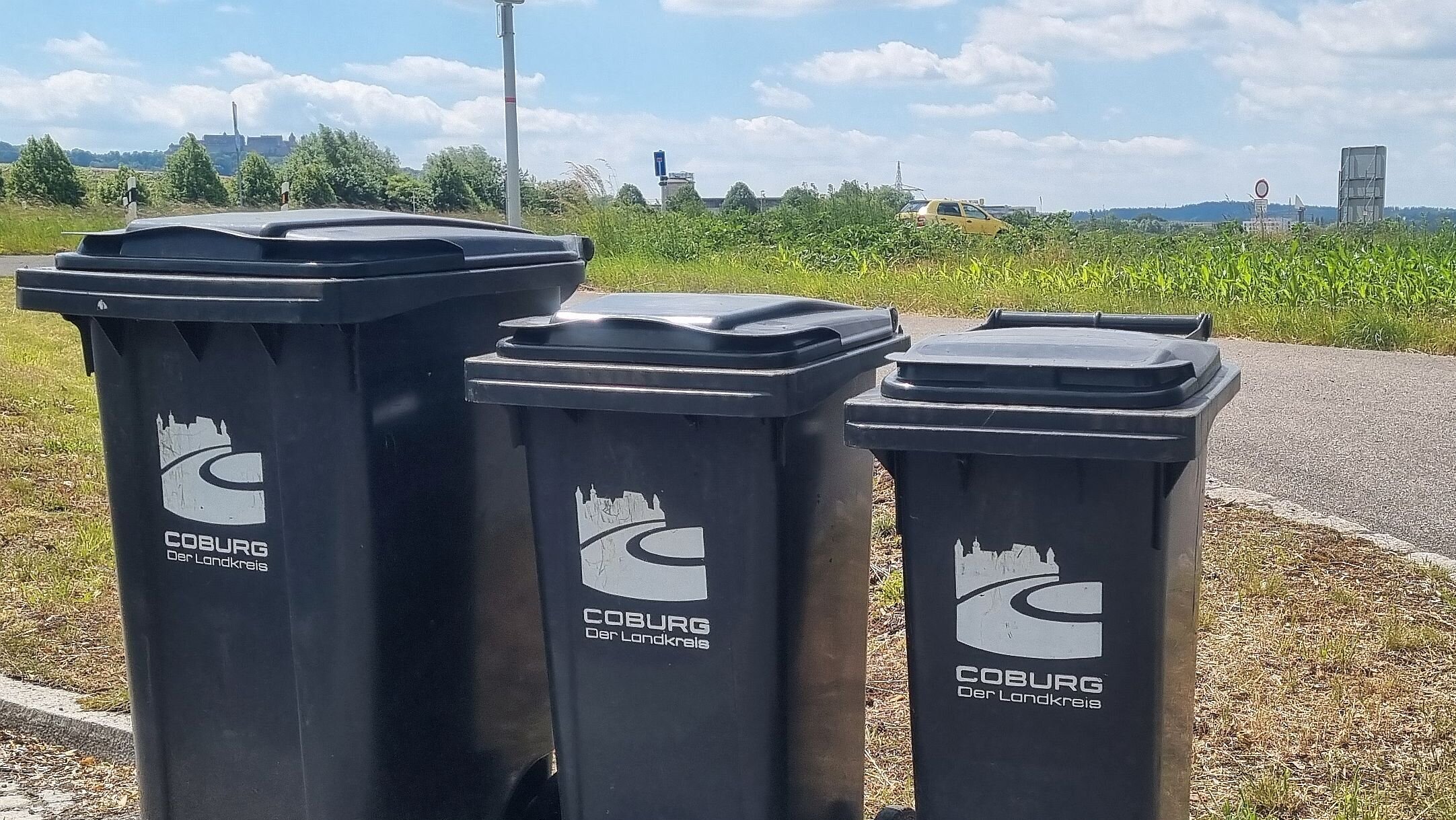Drei Mülltonnen mit dem Logo des Landkreises Coburg. Im Hintergrund ist am Horizont die Veste Coburg zu erkennen.