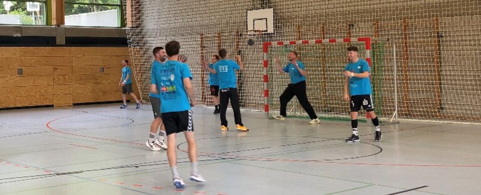 Jugendliche mit blauen Trikots spielen Handball in einer Sporthalle 