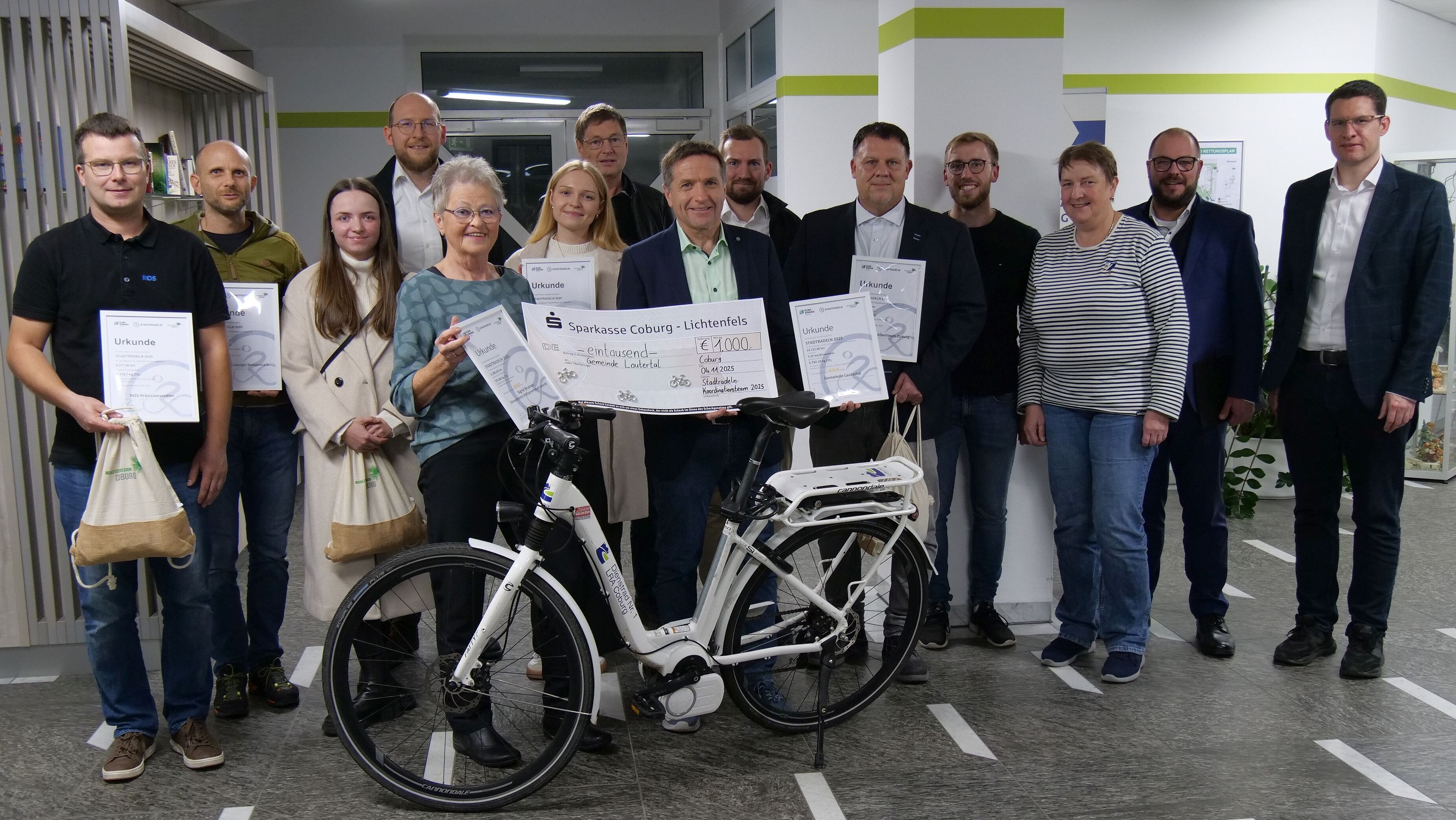 Gruppenbild mit allen Teilnehmern der Siegerehrung zum Stadtradeln 2025. Alle Handen ihre Urkunden und Sachpreise in der Hand, im Vordergrund steht symbolisch ein Fahrrad mit Landkreis-Logo auf dem Rahmen.