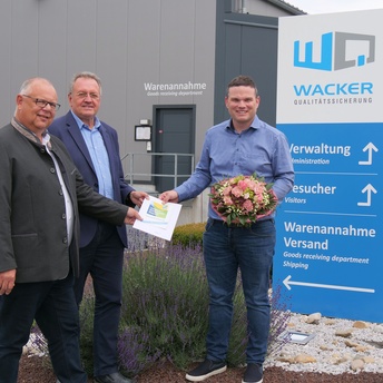 Martin Stingl, Udo Siegel und Markus Wacker neben einer Informationstafel am Haupteingang der Firma Wacker in Großheirath