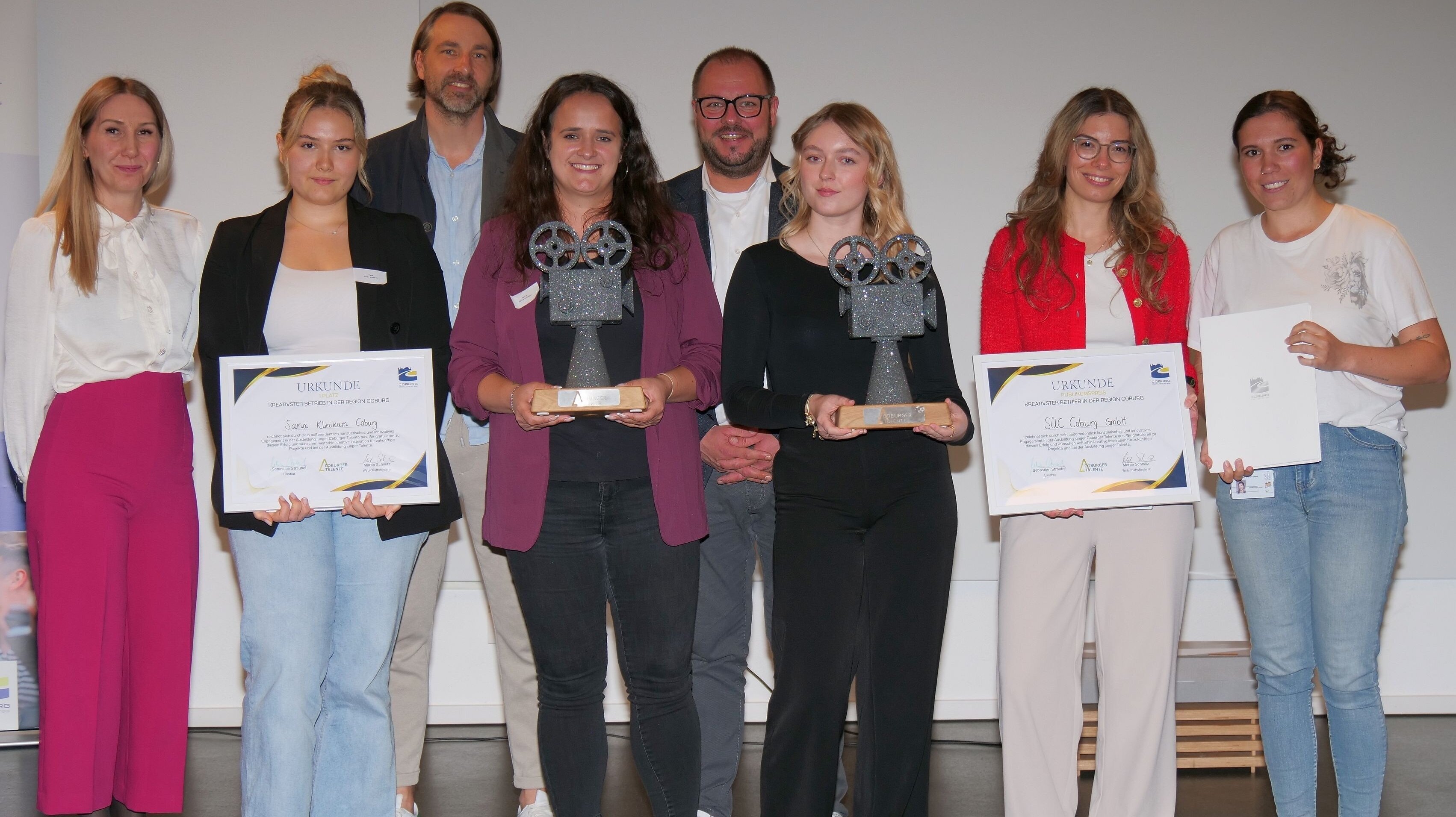 Die Gewinner des Video-Wettbewerbes. Sie halten die Siegerehrung und die Trophäen in Form einer Filmkamera in der Hand.