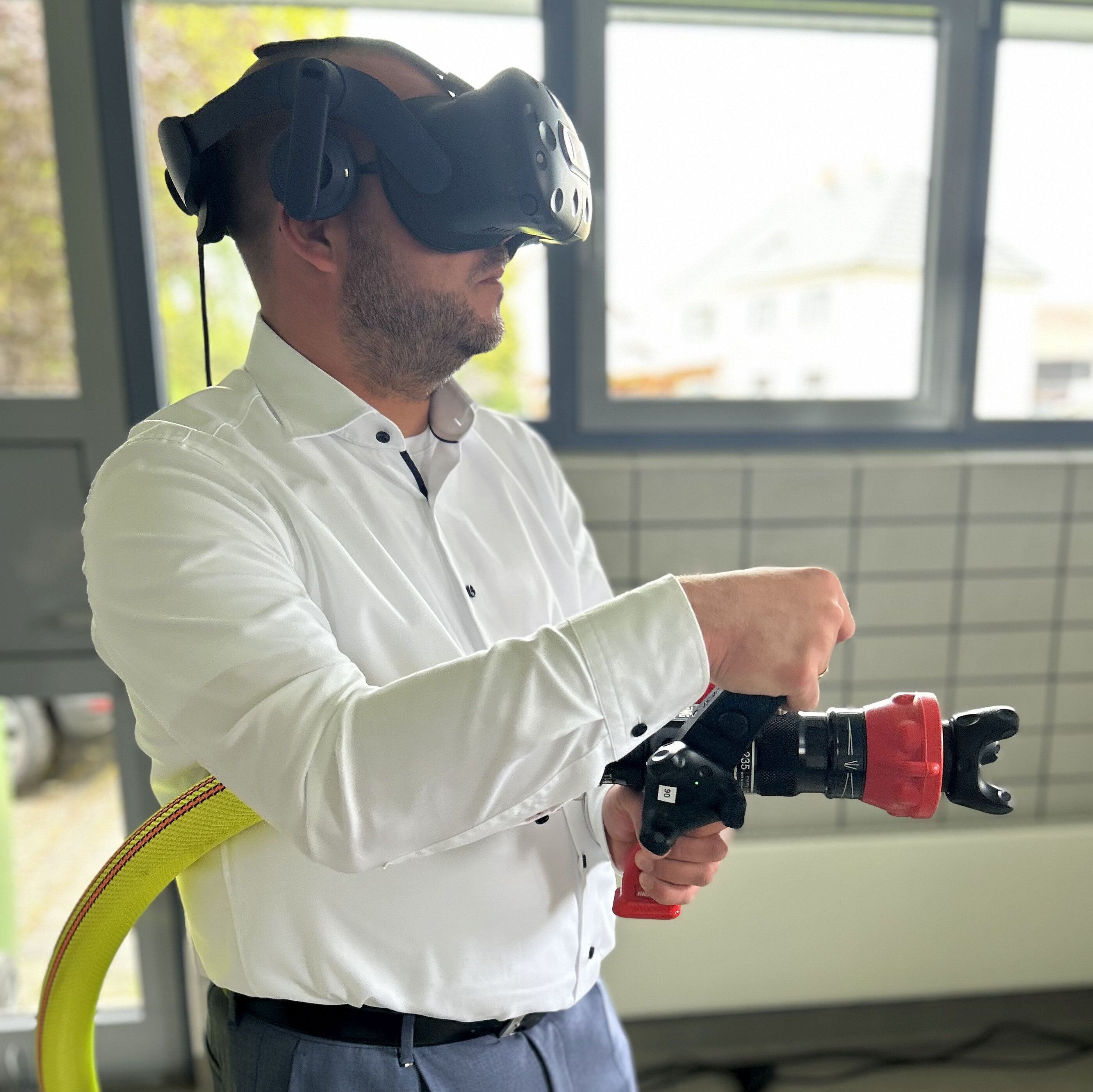 Landrat Sebastian Straubel mit einem Löschschlauch in der Hand. Er hat dabei eine VR-Brille auf dem Kopf