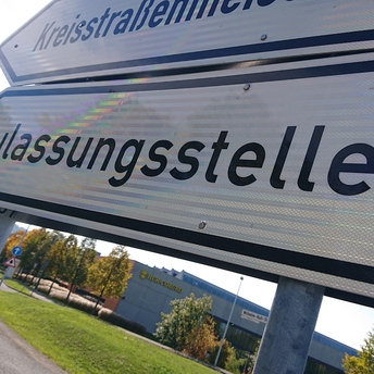 Blick auf ein Hinweisschild am Straßenrand mit der Aufschrift "Zulassungsstelle" 