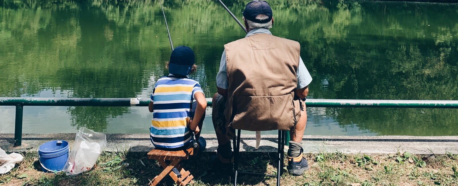 Ein Großvater sitzt mit seinem Enkel an einem See und angelt. 