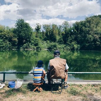 Ein Großvater sitzt mit seinem Enkel an einem See und angelt. 