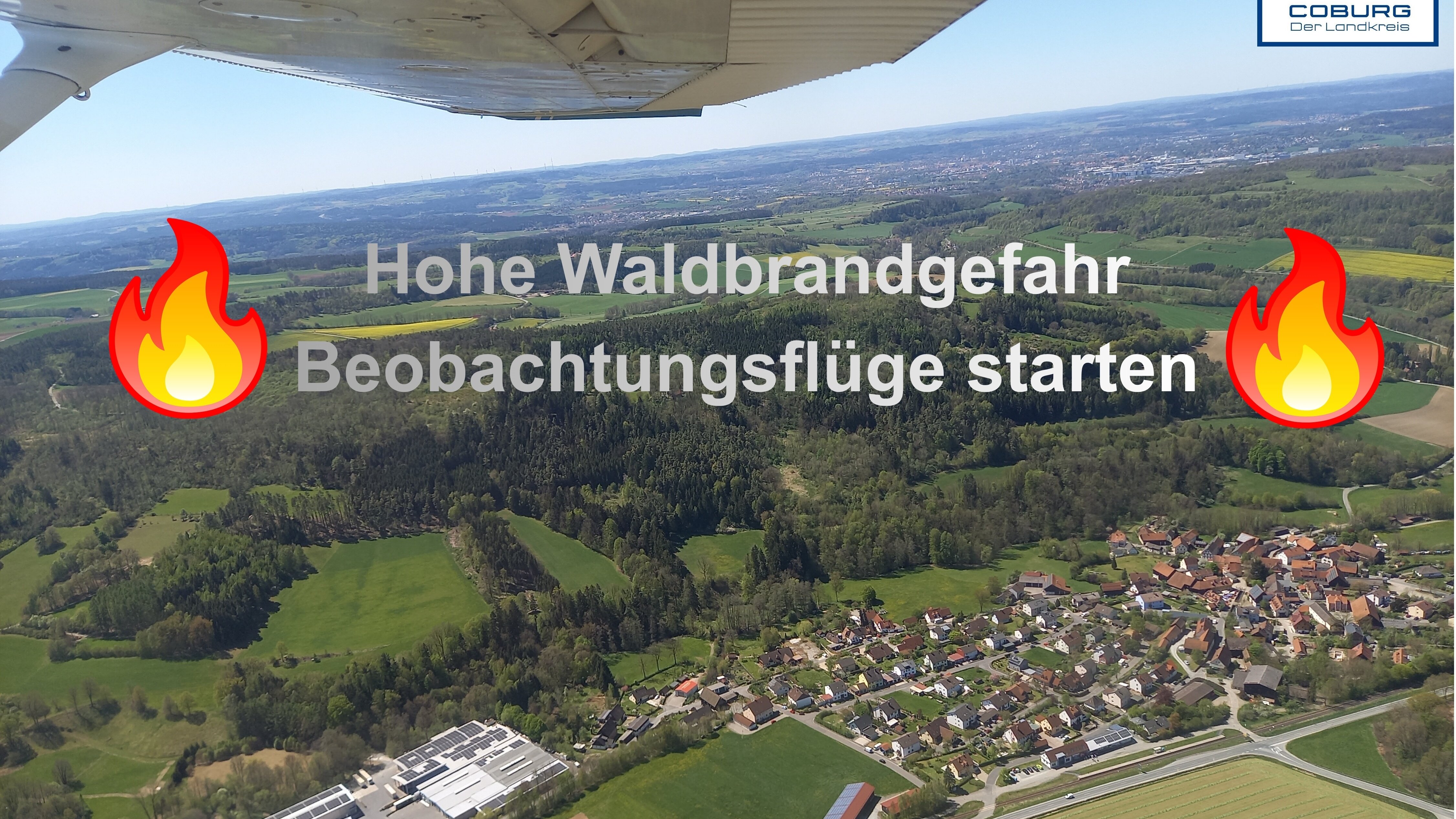 Luftaufnahme aus einem Flugzeug: Am Boden sind ein Waldstück sowie ein Wohngebiet zu sehen.