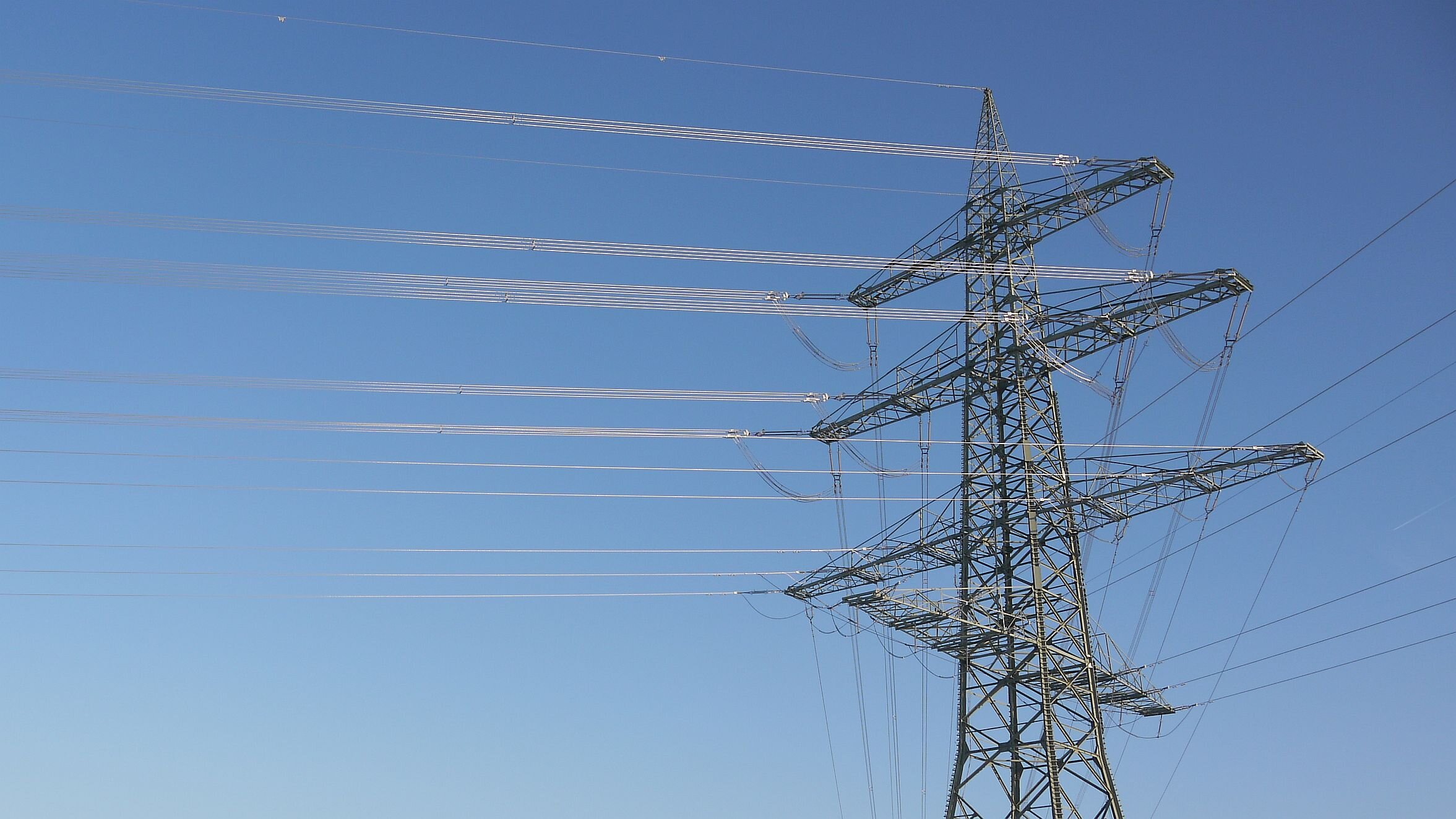 Ein Strommast mit Leitungen, die in der Sonne glänzen. Hintergrund ist strahlend blauer Himmel.