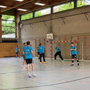 Jugendliche in blauen Trikots spielen in einer Sporthalle Handball. 