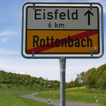 Das Schild am Ortsende von Rottenbach. Rottenbach ist rot durchgestrichen, oben steht Eisfeld mit einem Pfeil und der Angabe von sechs Kilometern Entfernung.