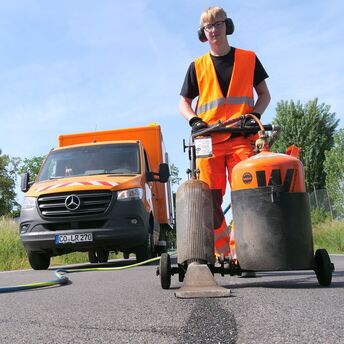 Ein Mitarbeiter der Straßenmeisterei bearbeitet mit einer Maschine eine Teerfläche. 