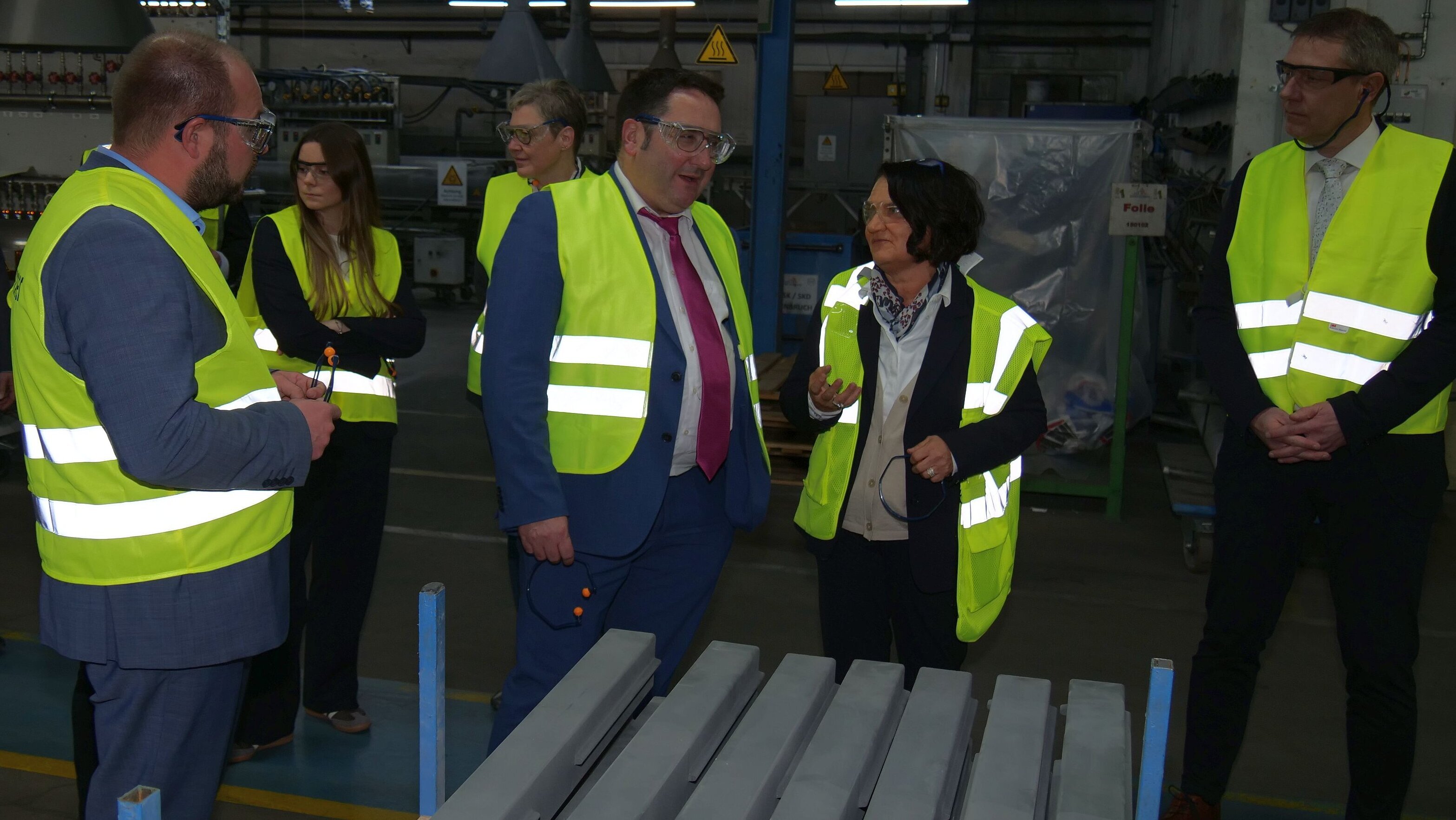 Eine Personengruppe bekleidet mit gelben Sicherheitswesten steht vor einem Regal mit dicken Platten aus grauer Industriekeramik. In der Mitte steht Geschäftsführerin Brigtte Wirth, die etwas erklärt.