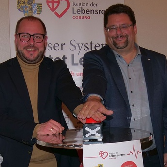 Stefan Wicklein und Sebastian Straubel drücken gemeinsam auf einen Buzzer-Knopf, um damit die Region der Lebensretter symbolisch zu starten.