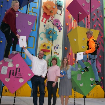 Im bunten Klettergarten der Funtasyworld hängen Stine Michel und Martin Lüders in Sicherungsseilen und reichen zwei Verträge an Sebastian Straubel und Yvonne Schnapp.