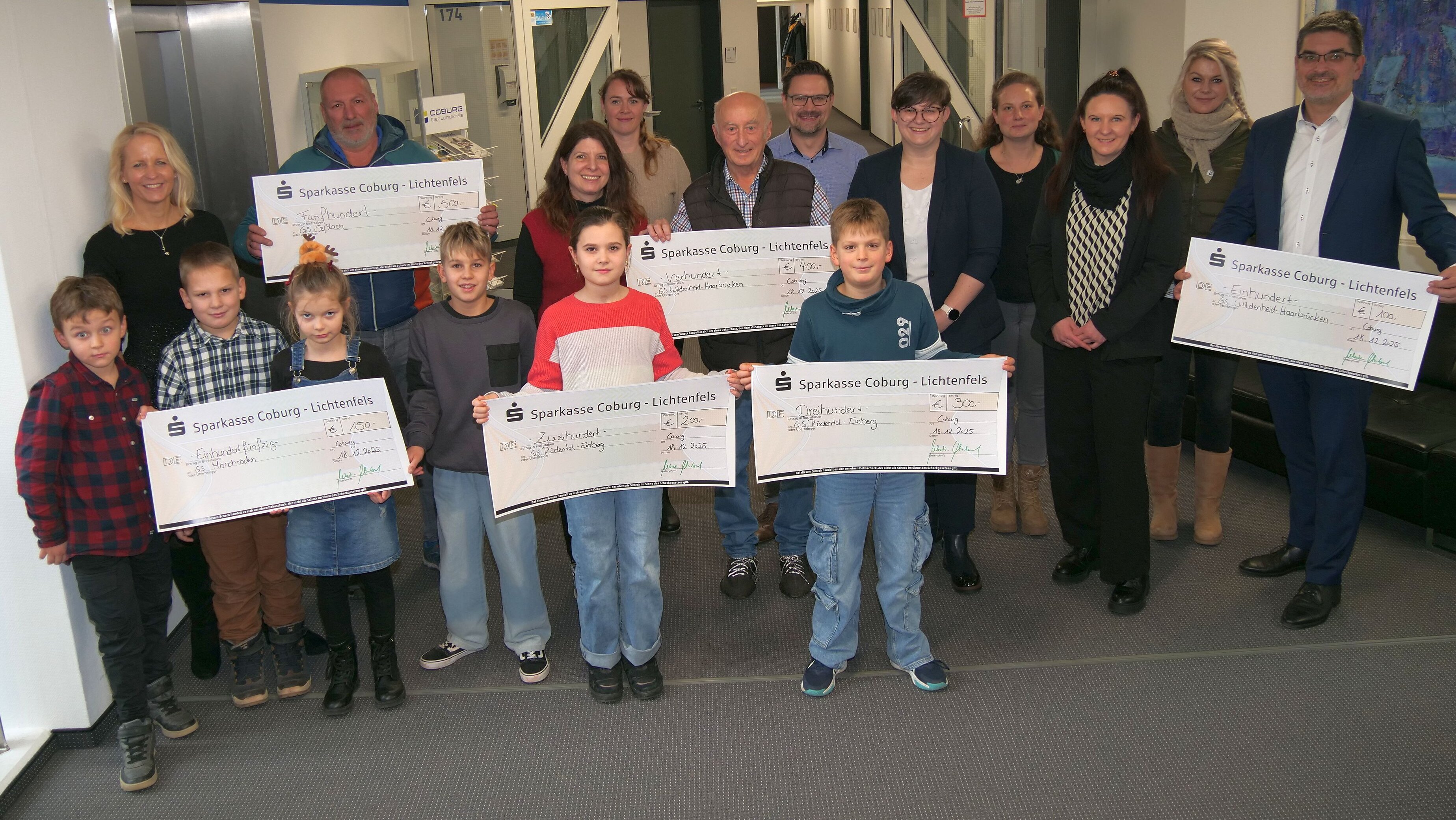 Beim Gruppenbild mit allen Schule steht vorne ein halbes Dutzend Kinder, die gemeinsam Spendenschecks in der Hand halten. Dahinter stehen die Erwachsenen.