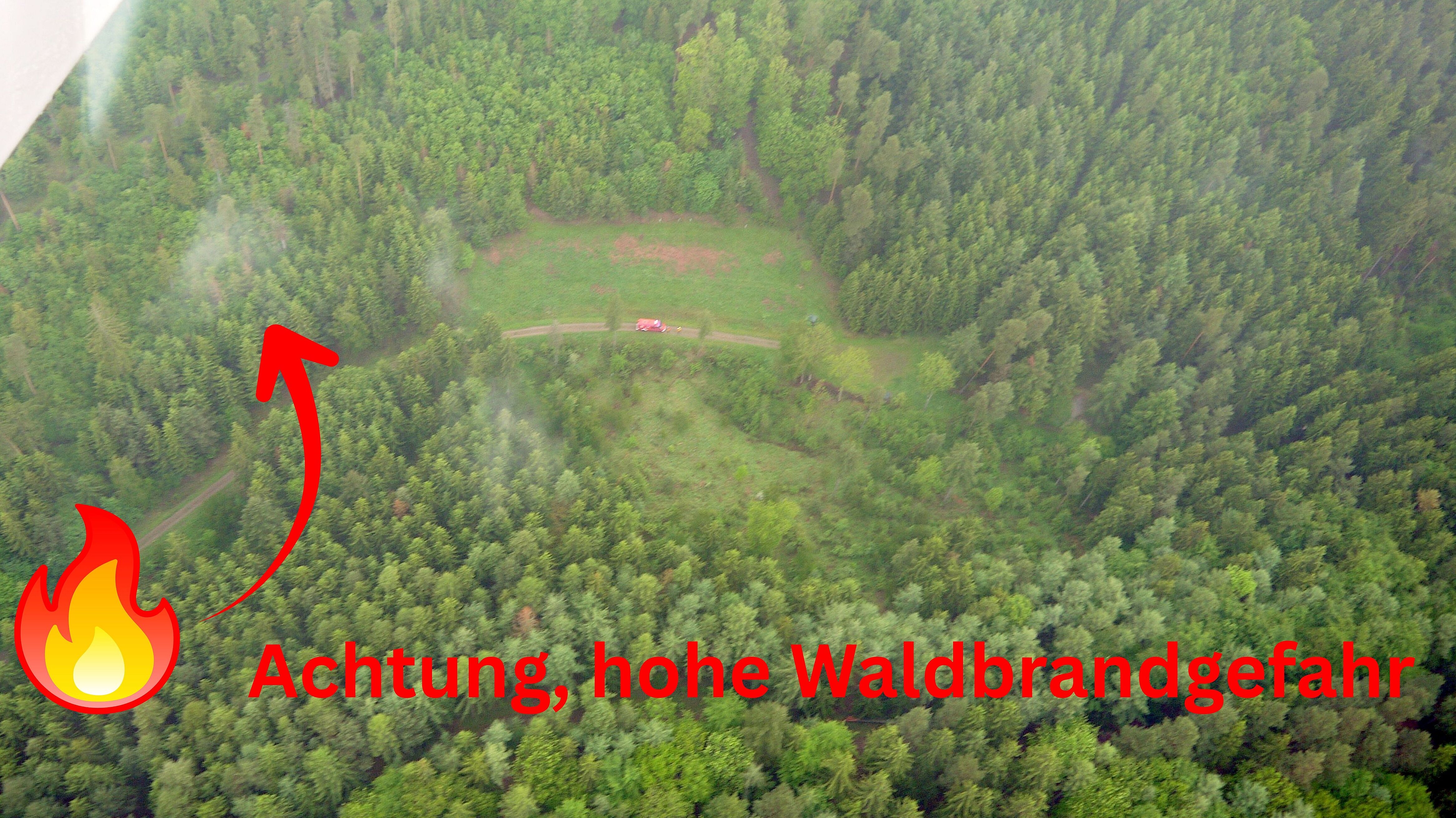 Aufnahme eines Waldgrundstückes von einem Flugzeug aus. Unten im Wald erkennt man eine kleine Rauchsäule.