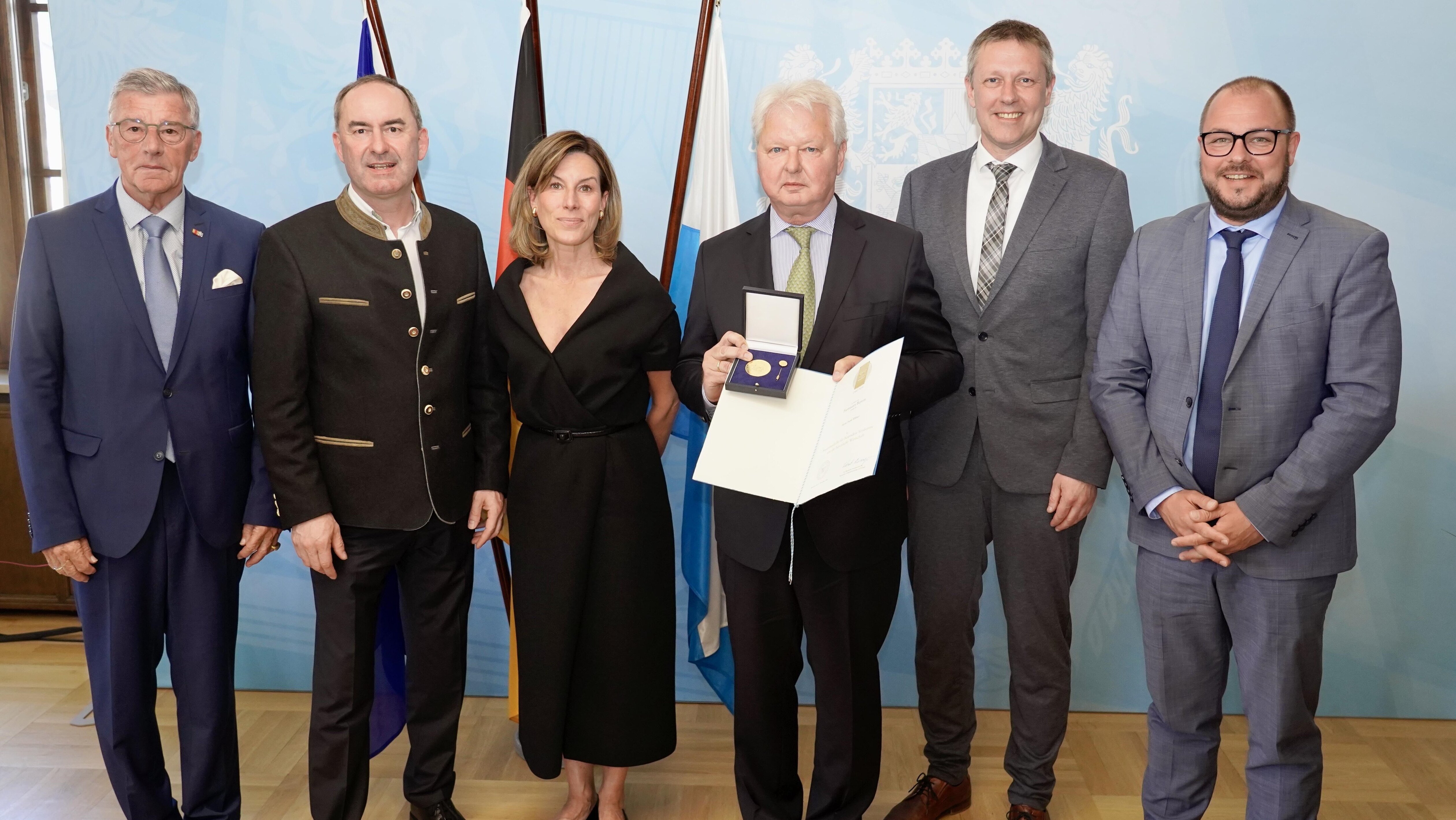 Frank Wöhner mit seiner Staatsmedaille in der Hand, umrahmt von Ehrengästen bei der Verleihung der Staatsmedaille.