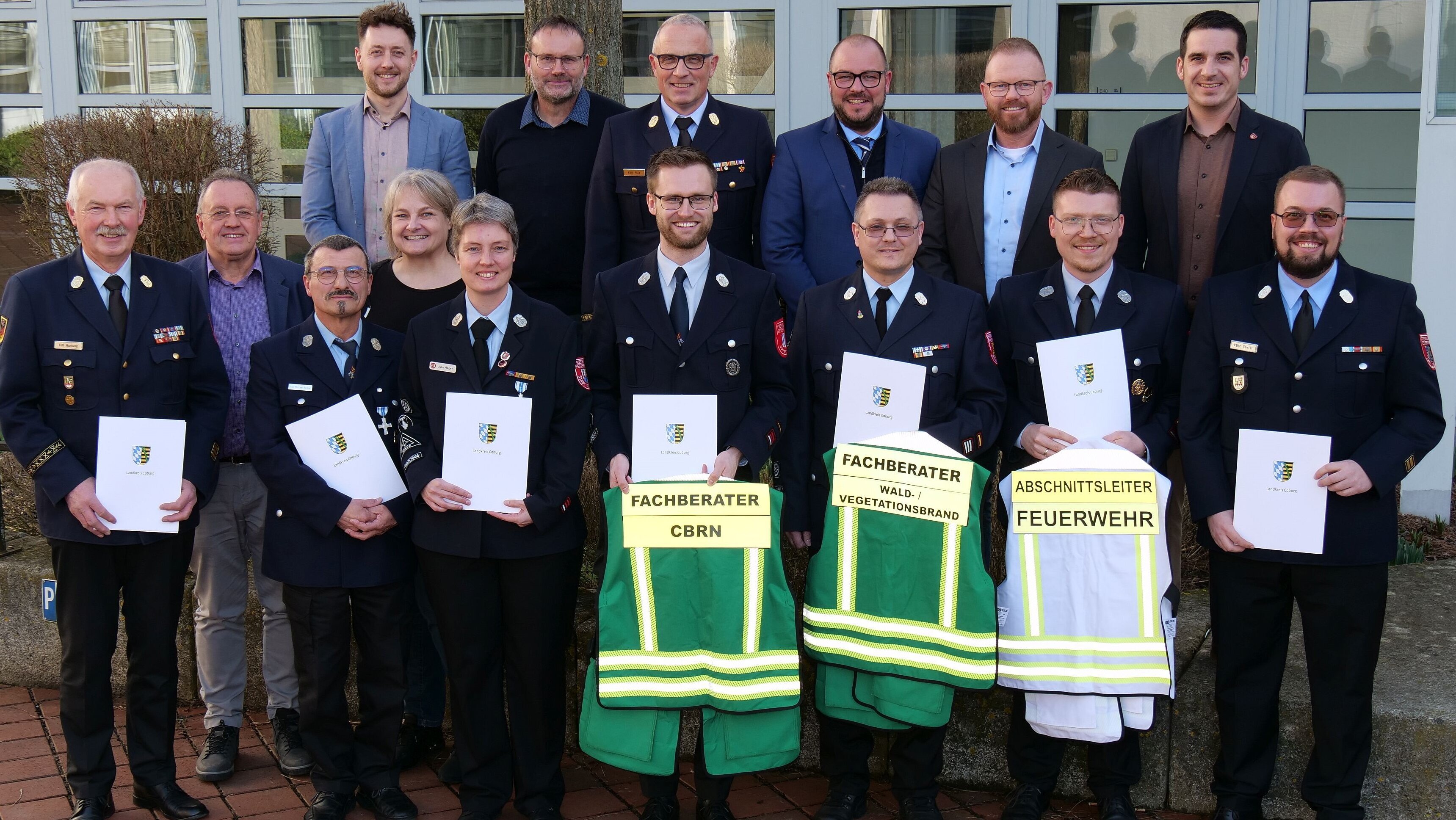 Gruppenbild mit 15 Personen. Vorne stehen Feuerwehr-Aktive in Uniform, die Urkunden in der Hand halten.