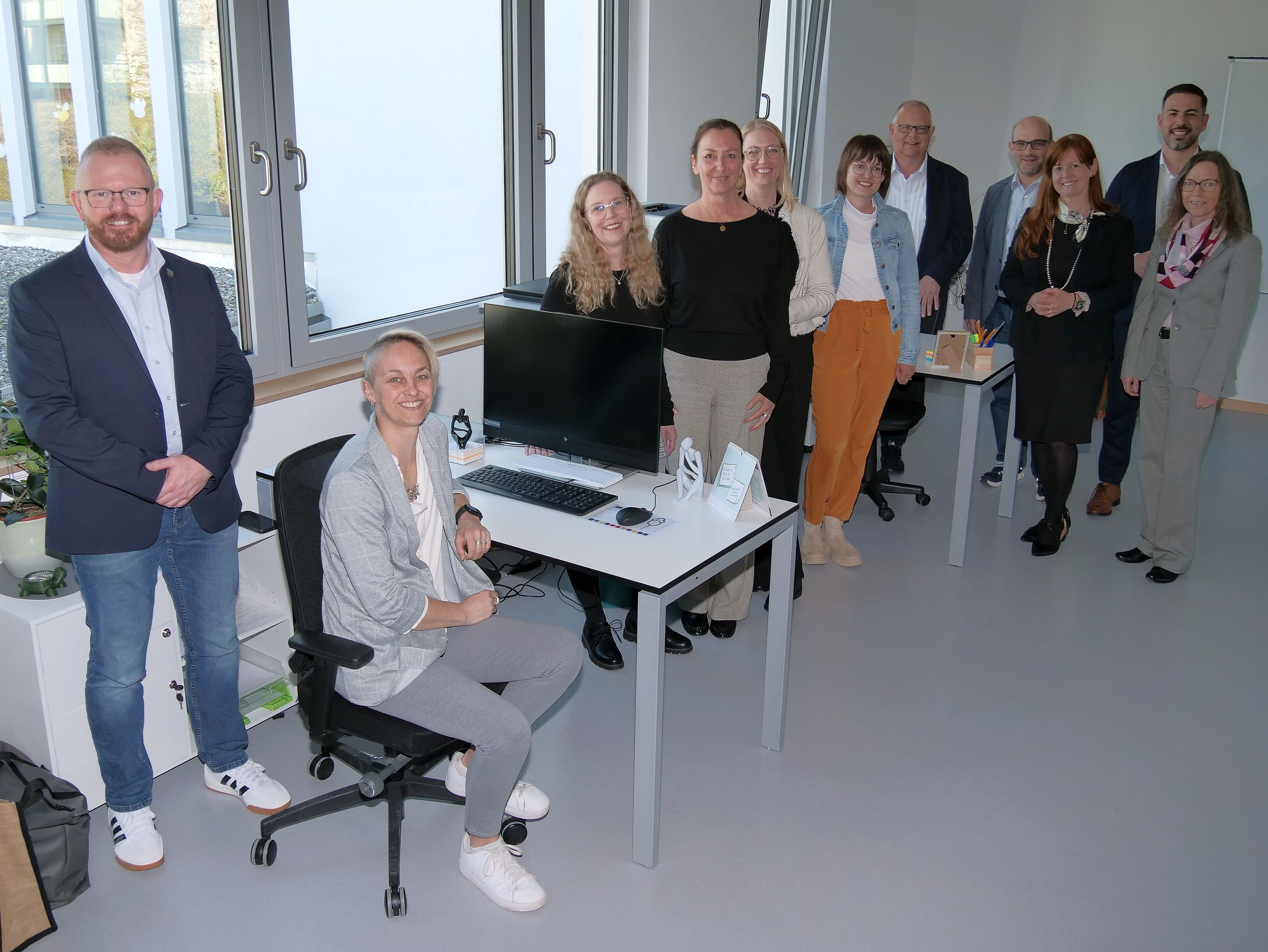 Elf Personen in einem Büro, drei davon gruppieren sich um einen Büro-Arbeitsplatzes. Das sind die neuen Mitarbeiterinnen des Mohritz-Büros.