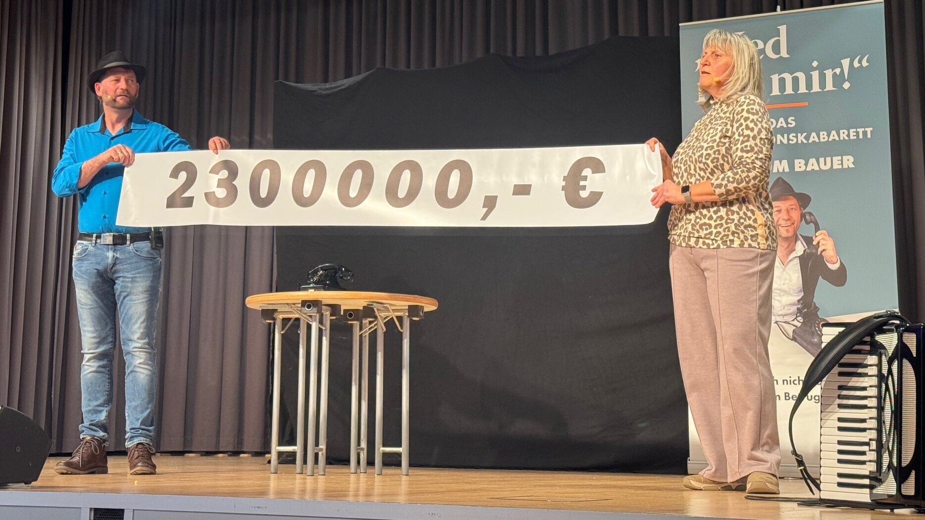 Zwei Personen halten ein Banner hoch, auf der die Summe von 2,3 Millionen Euro steht.