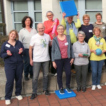 Eine Gruppe von Personen, die Bälle, Gumminudeln und kleine Hanteln für den Sport mit Senioren in der Hand halten.