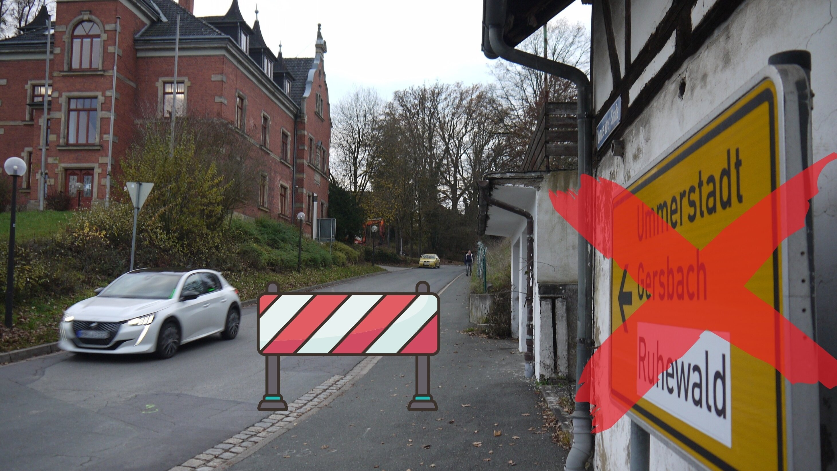 Die Kreisstraße CO 2 mit dem Rathaus der Gemeinde Weitramsdorf im Hintergrund. Vorne ist eine rot-weiße Absperrbake zu sehen.