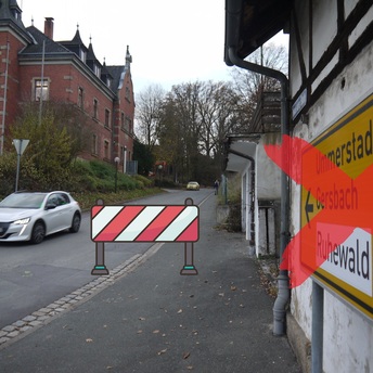 Die Kreisstraße CO 2 mit dem Gebäude des Weitramsdorfer Rathauses im Hintergrund. Vorne ist eine rot-weiße Absperrbake zu sehen.